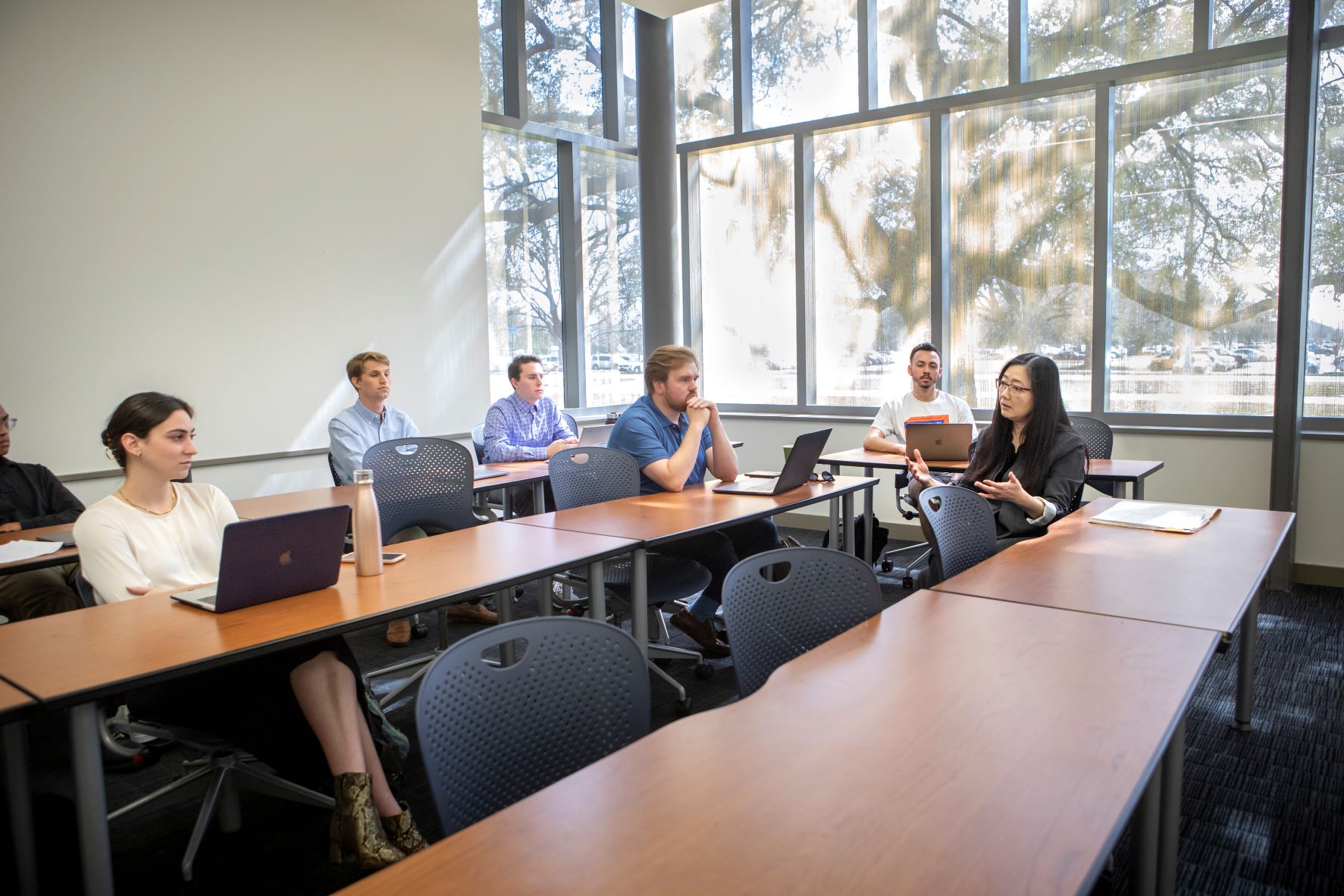 Professor sits with students while teaching class. 