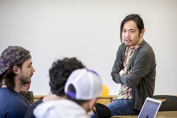 Professor sits on table and talks with students