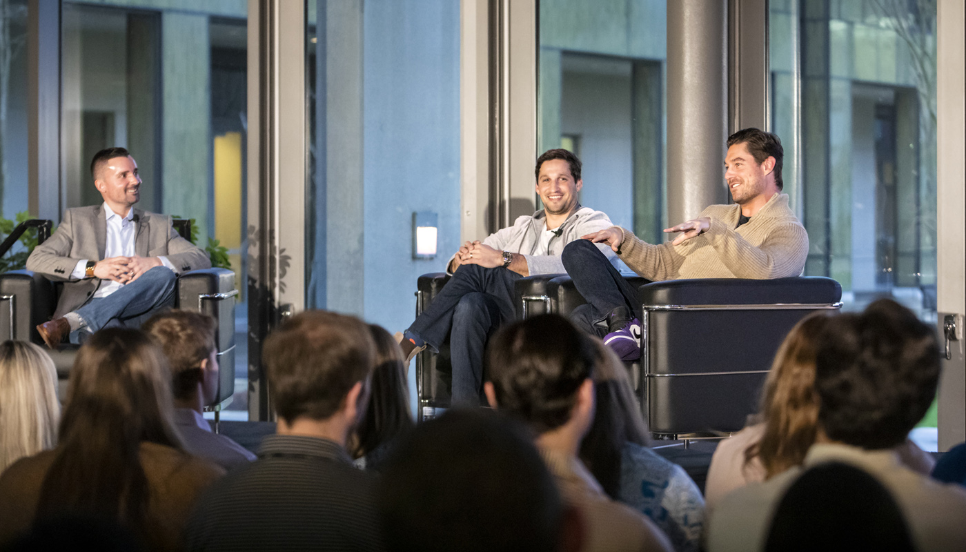 Three men sitting in chairs on a stage. 