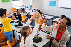 Photo of a teracher showing a young girls how to stack building blocks.