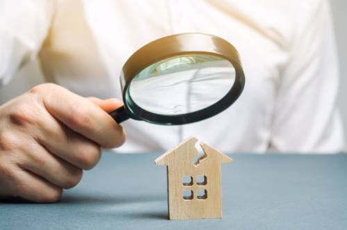 A hand holding a magnifying glass over a house